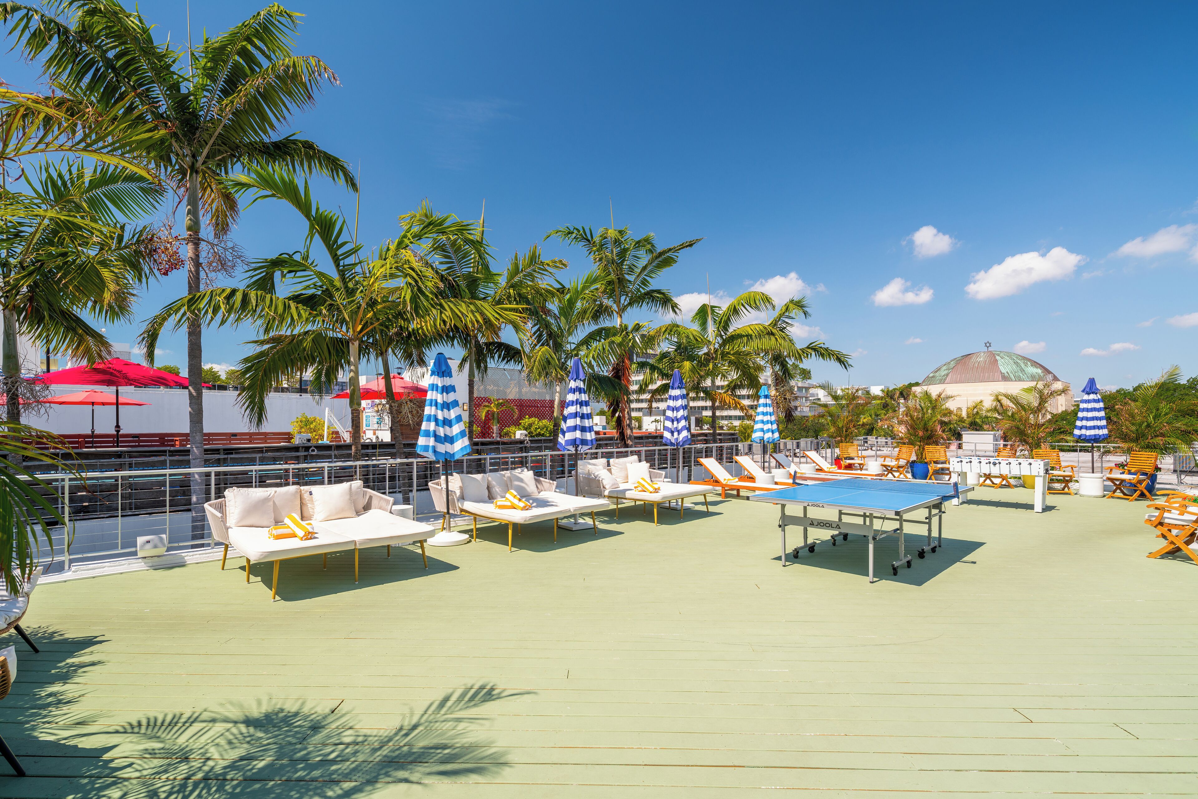 A rooftop deck with lounge chairs, umbrellas, and a ping pong table.