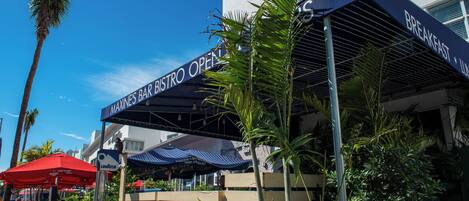 A restaurant with outdoor seating, palm trees, and a clear blue sky.
