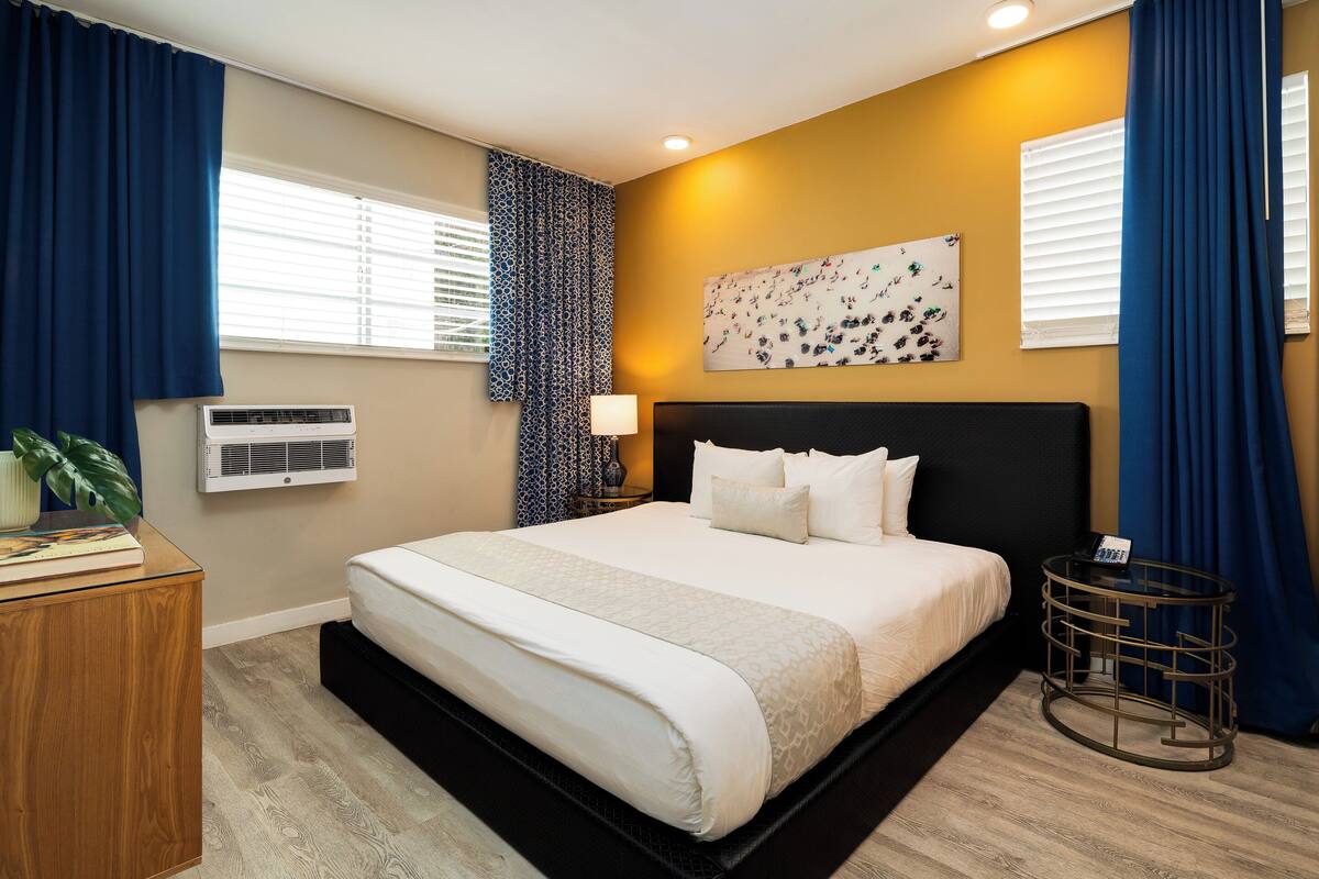 Une chambre d’hôtel bien aménagée, avec un grand lit, une table de chevet, une lampe et un climatiseur fixé au mur.