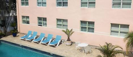 A hotel pool area with lounge chairs and a small table, surrounded by potted plants.