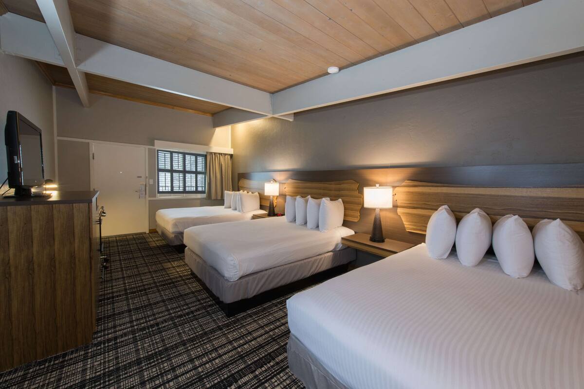 A hotel room with two beds, a wooden desk, a television, and a window with curtains.