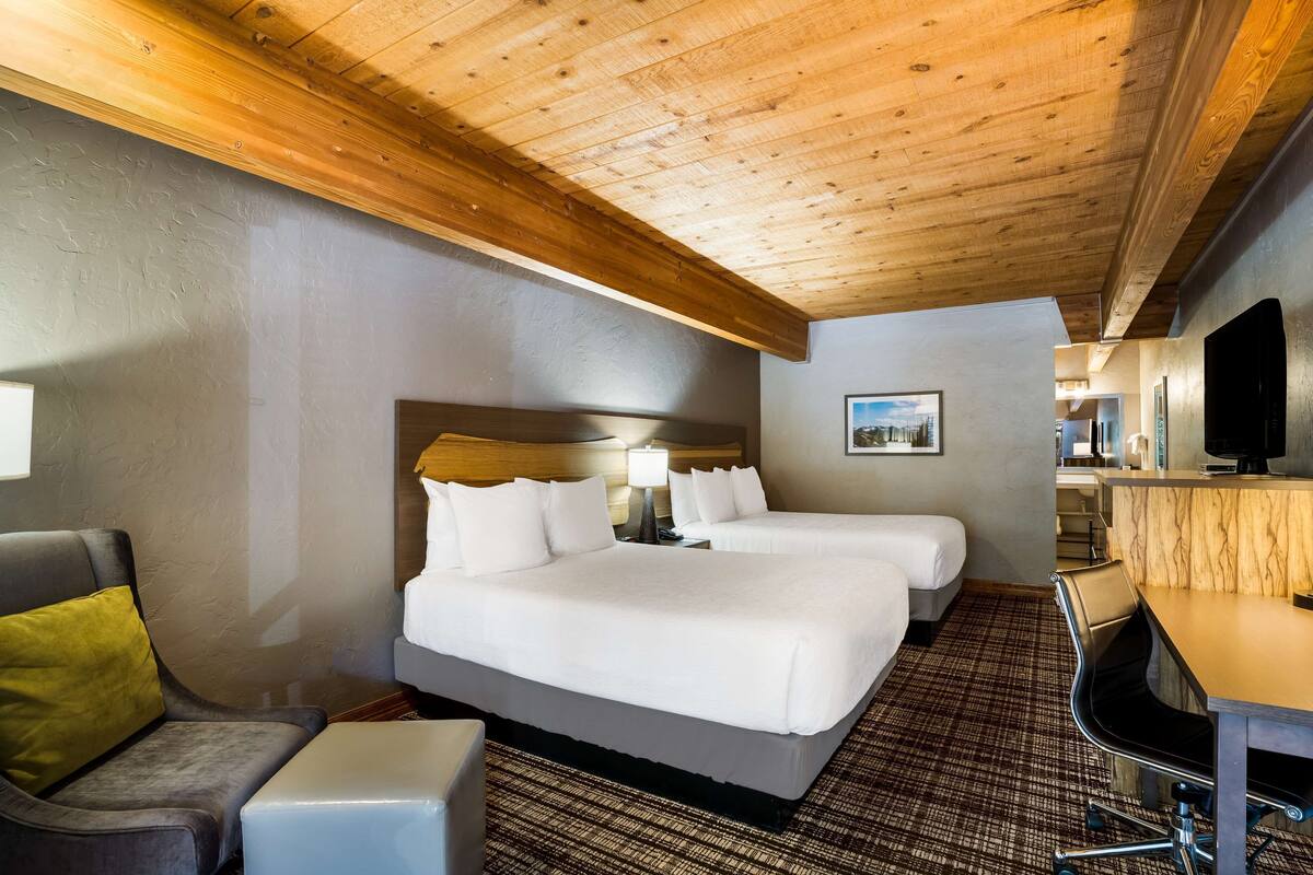 A hotel room with two beds, a desk, a chair, and a television.