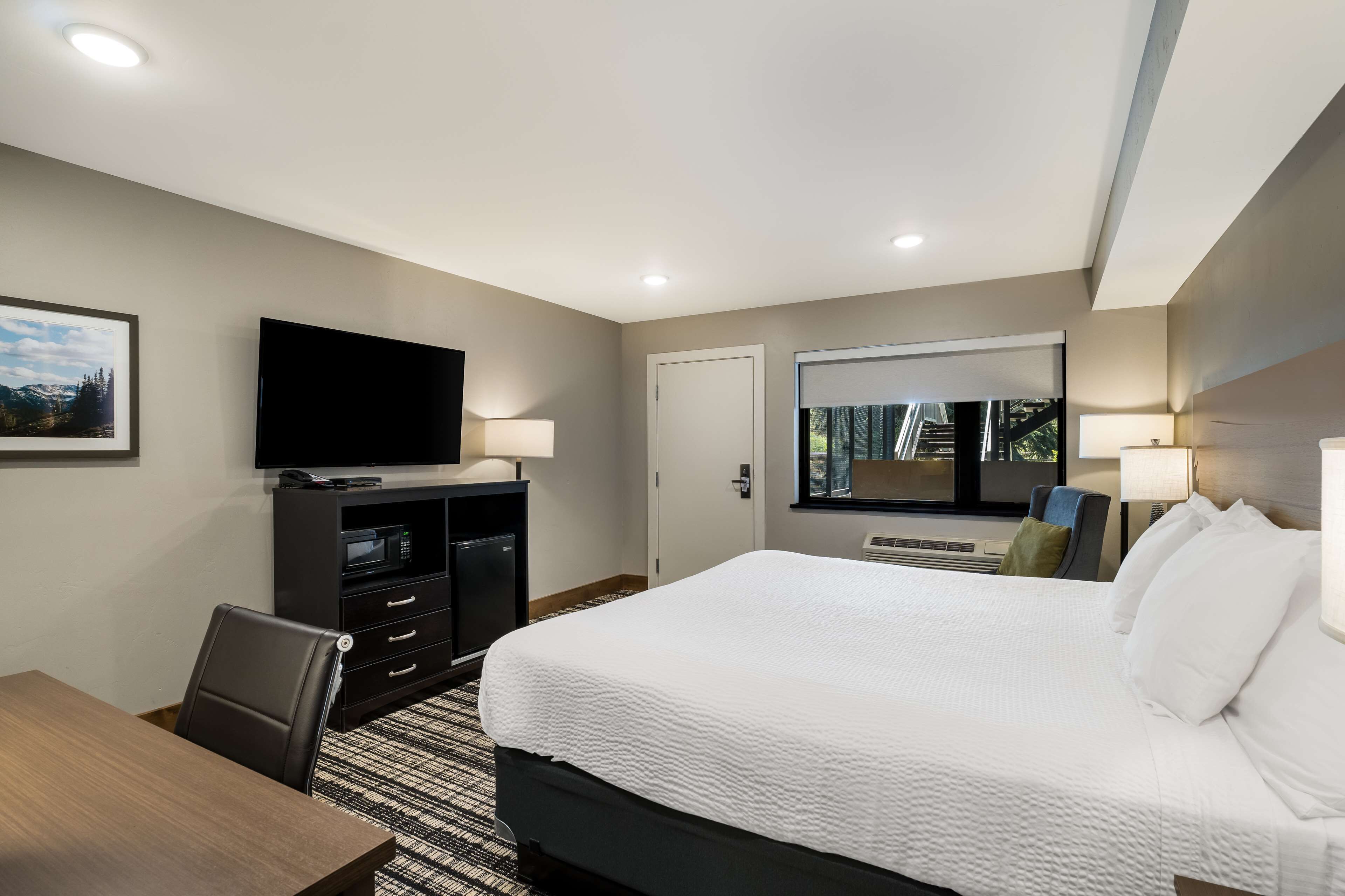 A hotel room with a large bed, a flat-screen TV, a desk with a chair, and a window with a view of the outdoors.
