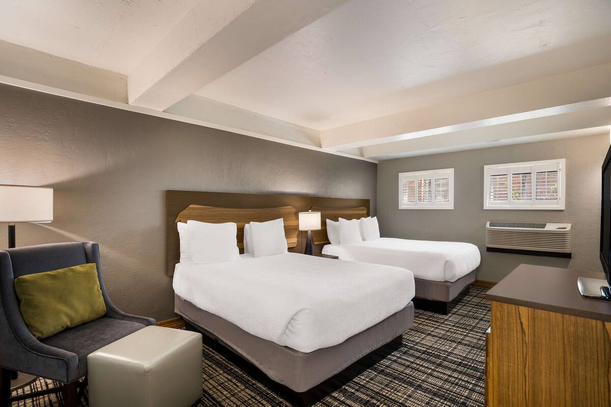 A hotel room with two beds, a desk, a chair, and a TV.