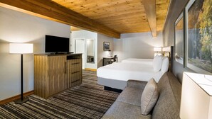 Een hotelkamer met een houten plafond, een groot bed, een bank, een televisie op een houten kast en een schilderij aan de muur.