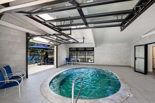 Piscina interna com teto de vidro, cadeiras azuis e vista para o exterior.