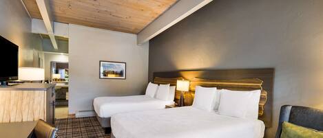 A hotel room with two beds, a desk, a chair, and a television.