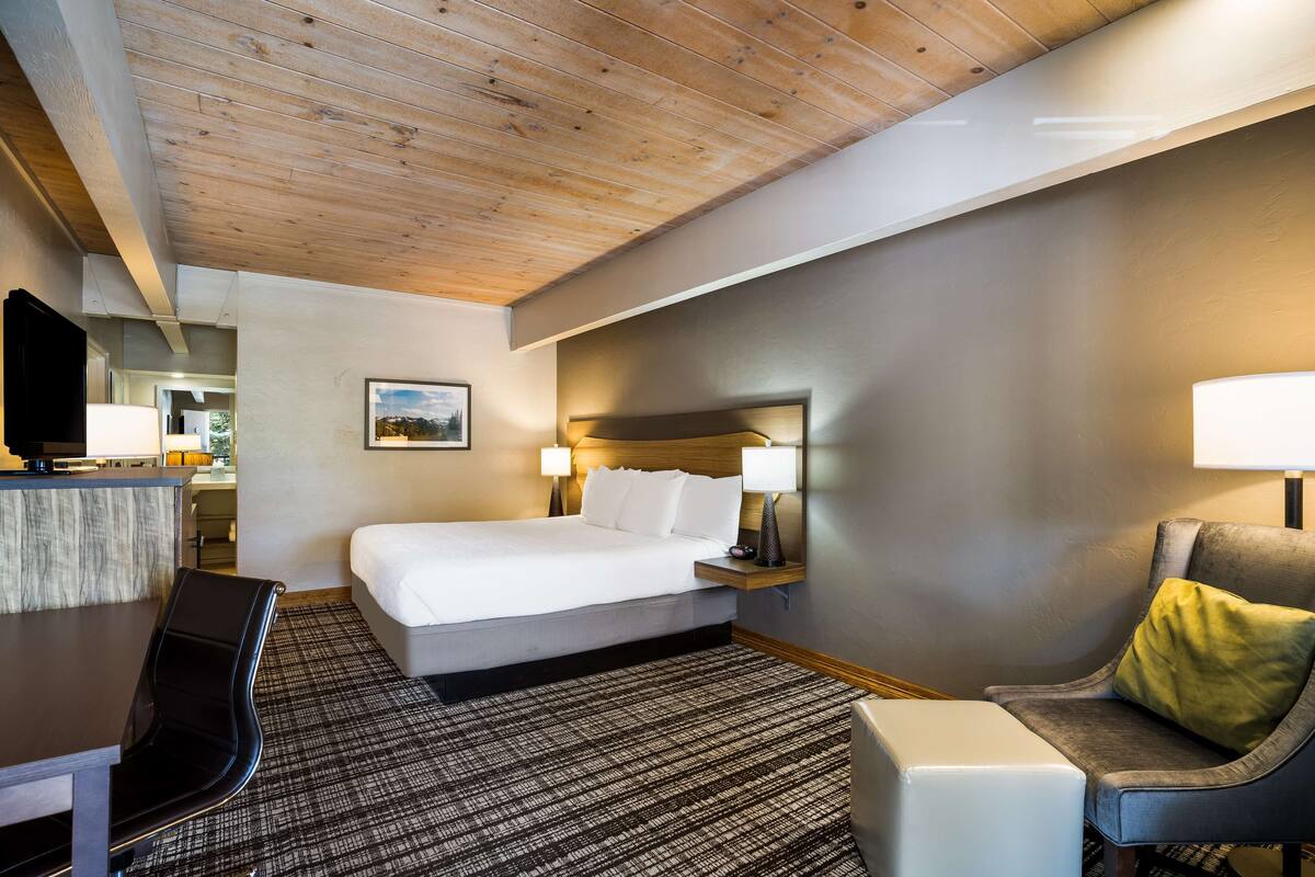 A hotel room with a bed, a desk, a chair, and a television.