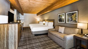 Een hotelkamer met een houten plafond, een groot bed, een bank, een bureau met een lamp en twee ingelijste foto's aan de muur.