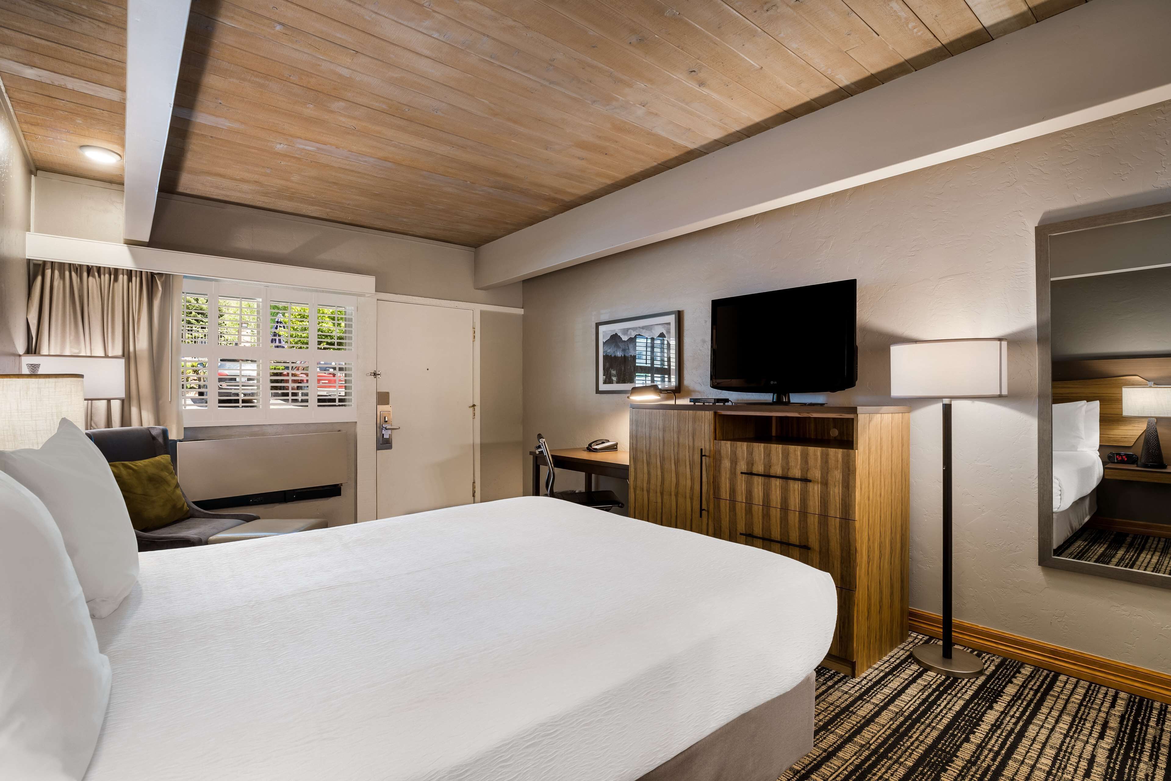 Una habitación de hotel con una cama grande, un televisor de pantalla plana en la pared, un escritorio con una silla y un armario.