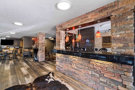 A bar area with a stone wall, wooden flooring, and hanging pendant lights.