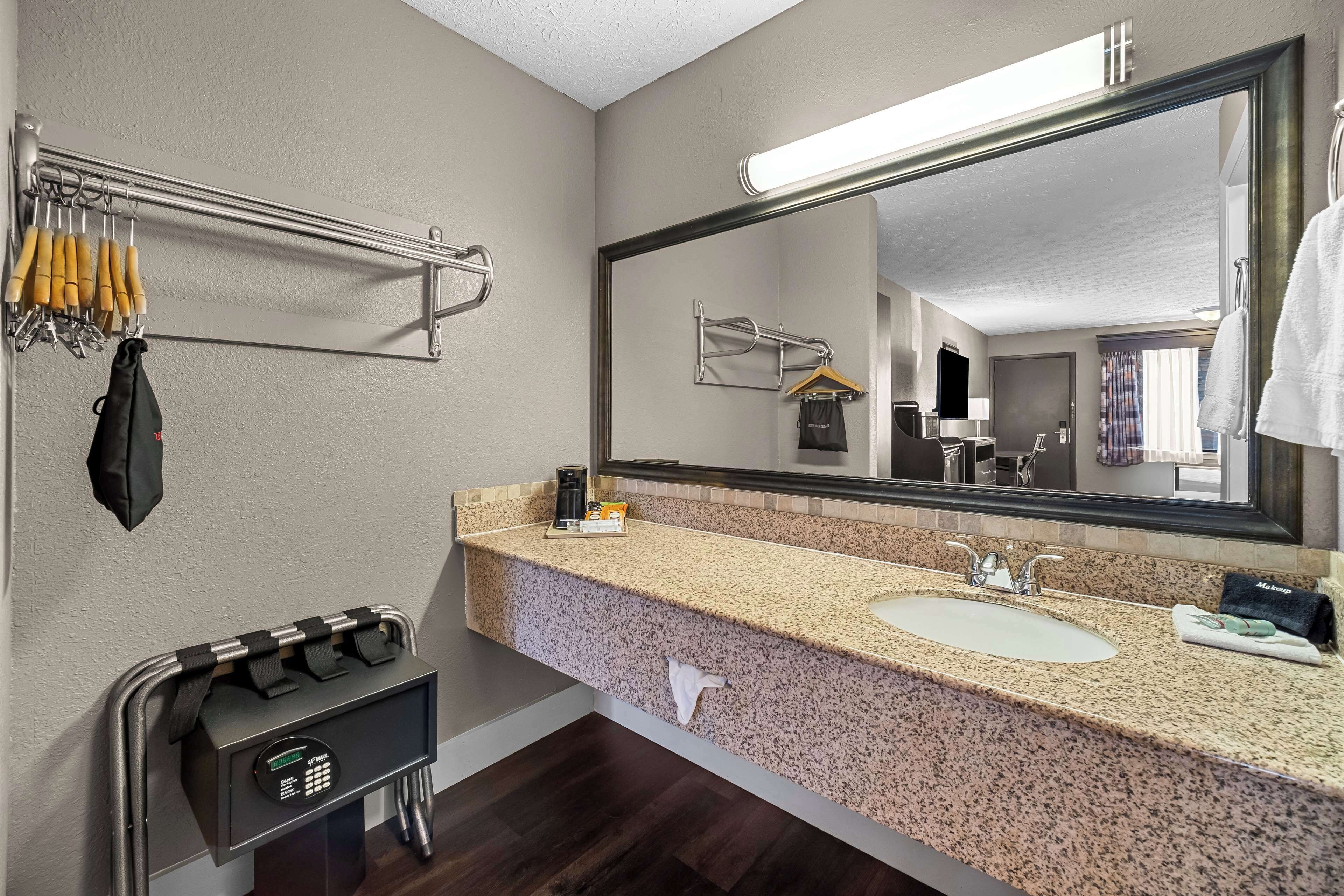 Un baño de hotel con lavamanos de encimera de granito, un espejo grande y un perchero con ganchos.