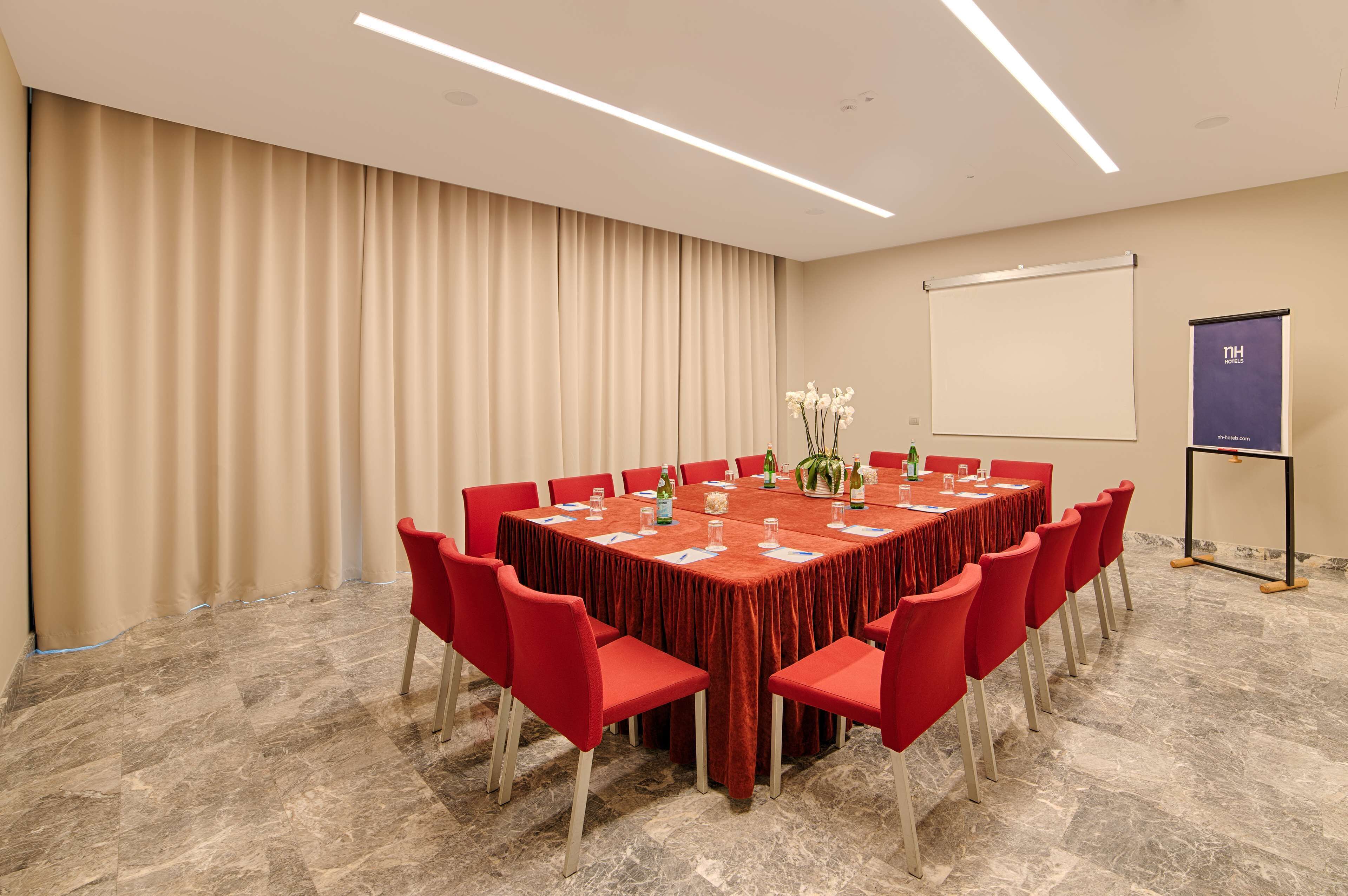 Een vergaderzaal met een ronde tafel, rode stoelen, een projectiescherm en een spandoek.