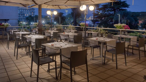 Een terras met tafels en stoelen, overdekt en met uitzicht op een stadslandschap.