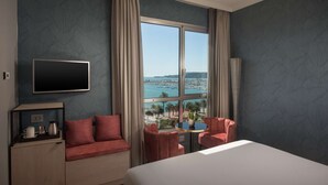 Een hotelkamer met een bed, een televisie, een bureau met een koffiezetapparaat, een stoel en uitzicht op zee.