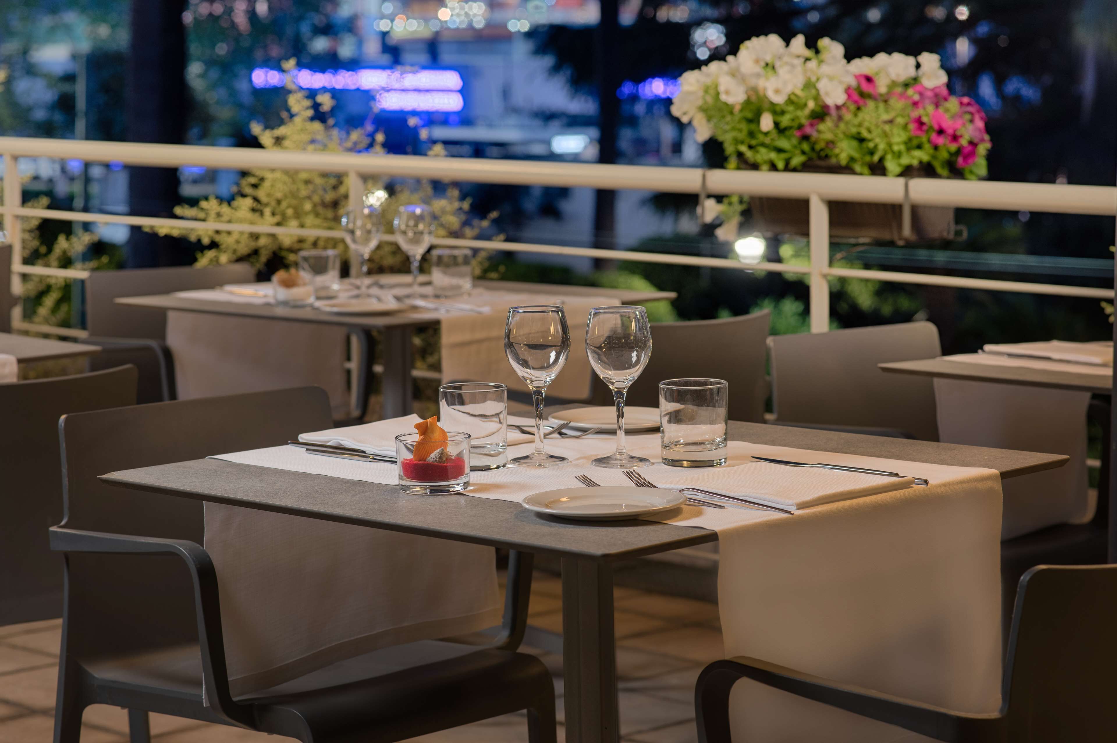 A restaurant with tables set for dining, featuring a city view at night.