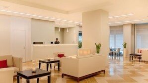 Een moderne hotellobby met een receptiebalie, een zithoek en grote ramen.