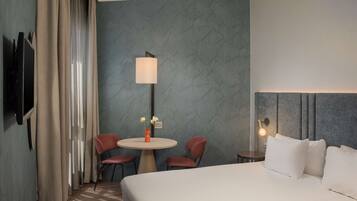 A hotel room with a bed, a round table with chairs, a lamp, and a TV mounted on the wall.