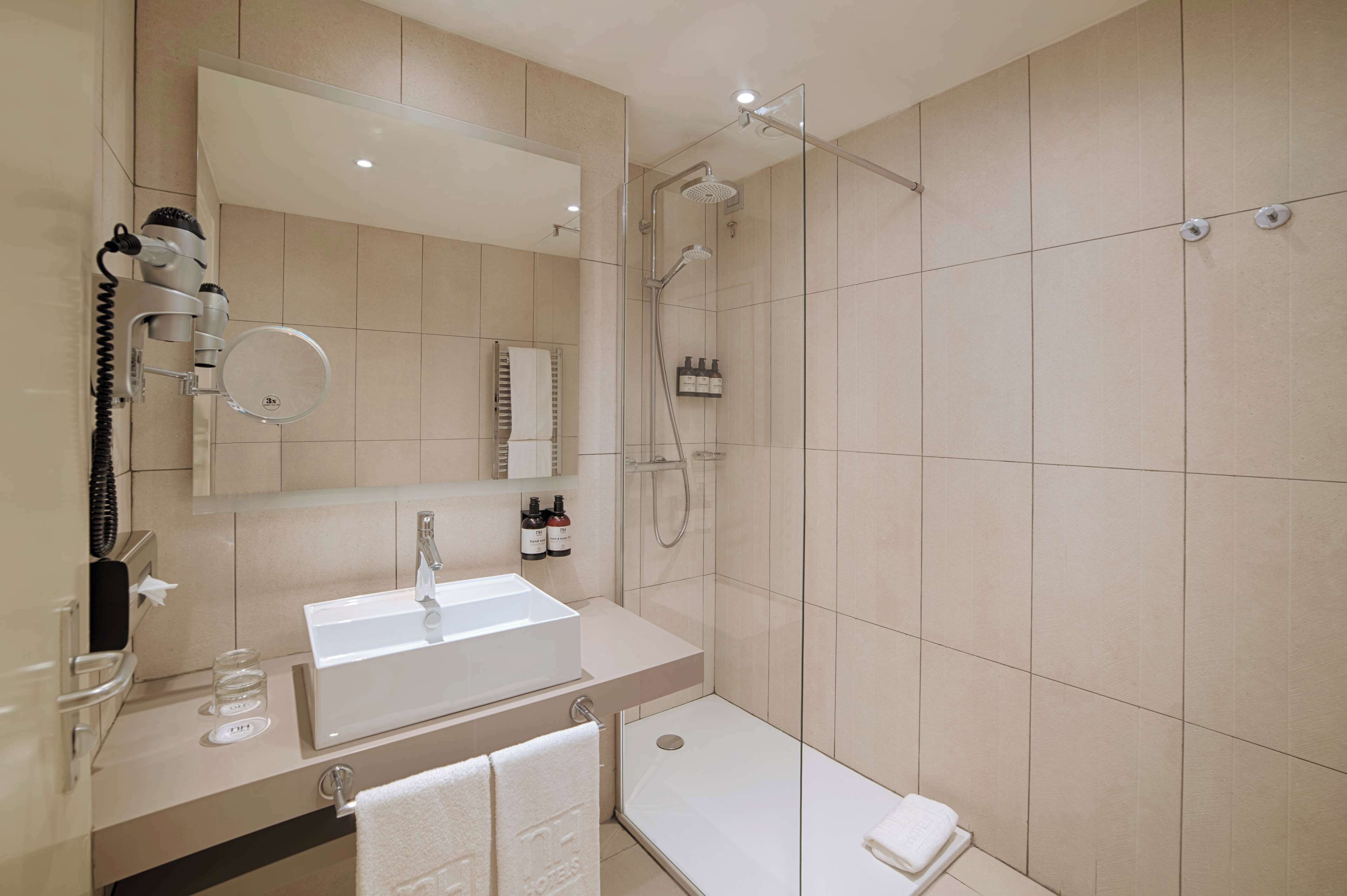 Une salle de bain moderne équipée d’un lavabo, d’un miroir, d’un sèche-cheveux et d’une douche.