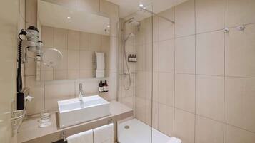Une salle de bain moderne équipée d’un lavabo, d’un miroir, d’un sèche-cheveux et d’une douche.