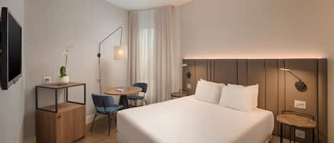 Een hotelkamer met een groot bed, een bureau met stoel, een klein tafeltje, een potplant en een televisie.