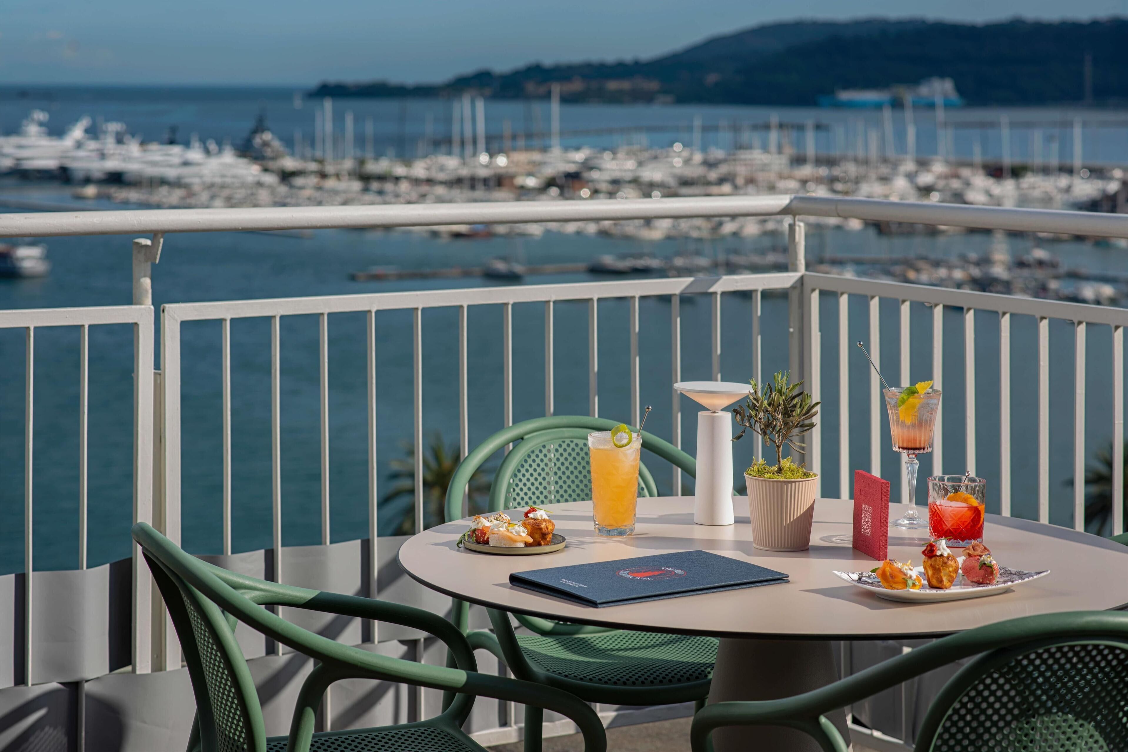 Varanda com mesa posta para dois, com vista para uma marina e barcos.