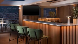 Een moderne buitenbar met een houten achtergrond, een flatscreen televisie en barstoelen.