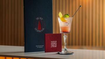 A cocktail glass with a lemon twist garnish on a bar counter, a QR code, and a menu titled "The Red Lighthouse" next to it.