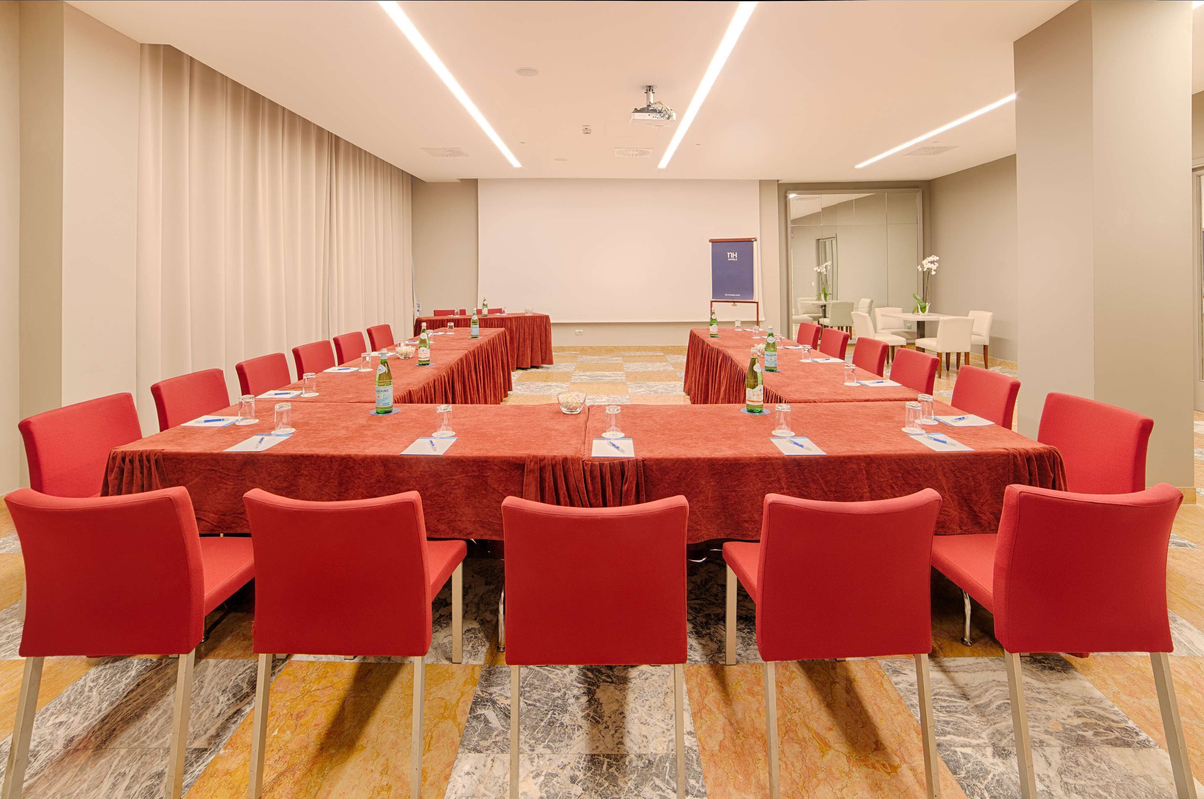 Una sala de conferencias con una gran mesa ovalada, sillas rojas y una pantalla de proyector.