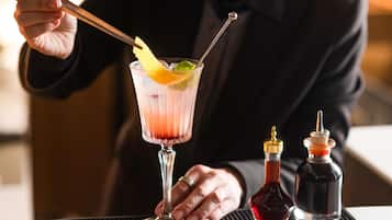 En bartender som blandar en cocktail med hjälp av en shaker, ett glas och två flaskor sås, allt placerat på en barbricka.
