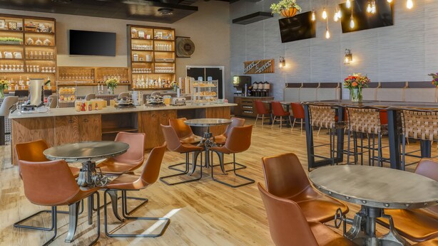 A modern bar area with wooden shelves, leather chairs, and a variety of bottles and glasses.