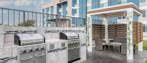 A barbecue area with a grill and oven, outdoor seating, and a Marriott hotel in the background.
