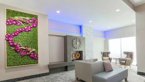 A modern lobby with a green wall art, a grey sofa, and a large clock.