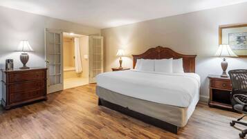 Une chambre d’hôtel avec un grand lit, des tables de chevet en bois, un bureau avec une chaise et une porte donnant sur une salle de bain.
