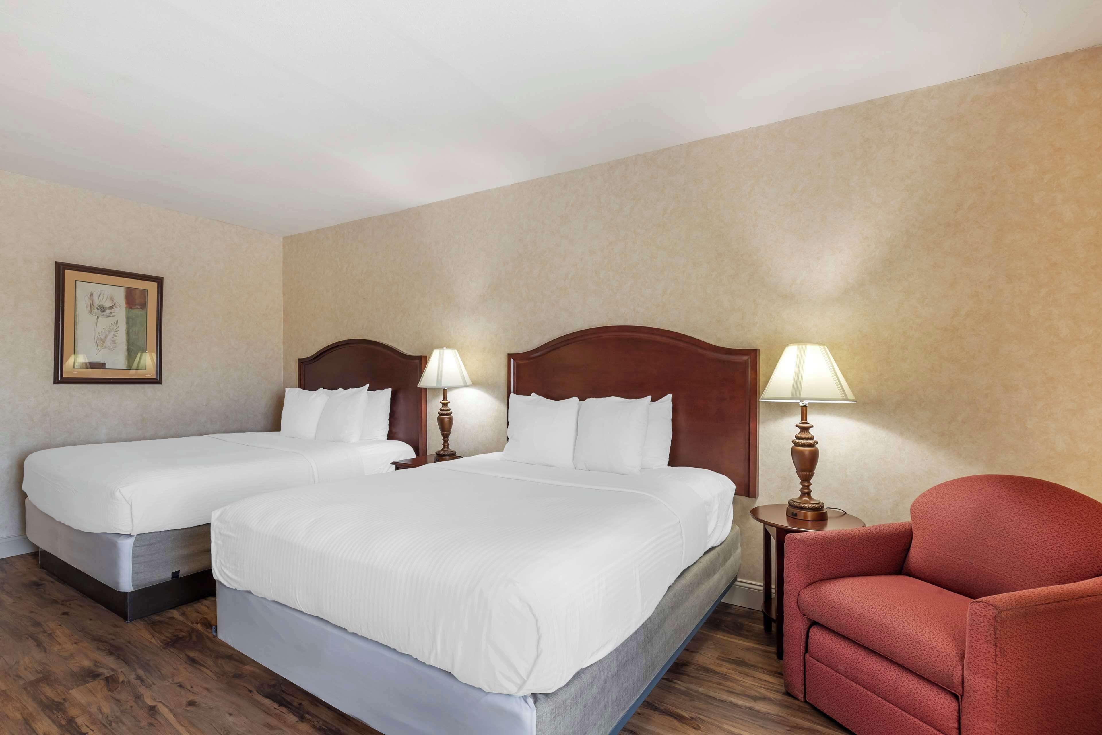 A hotel room with two beds, a red armchair, and two bedside lamps.