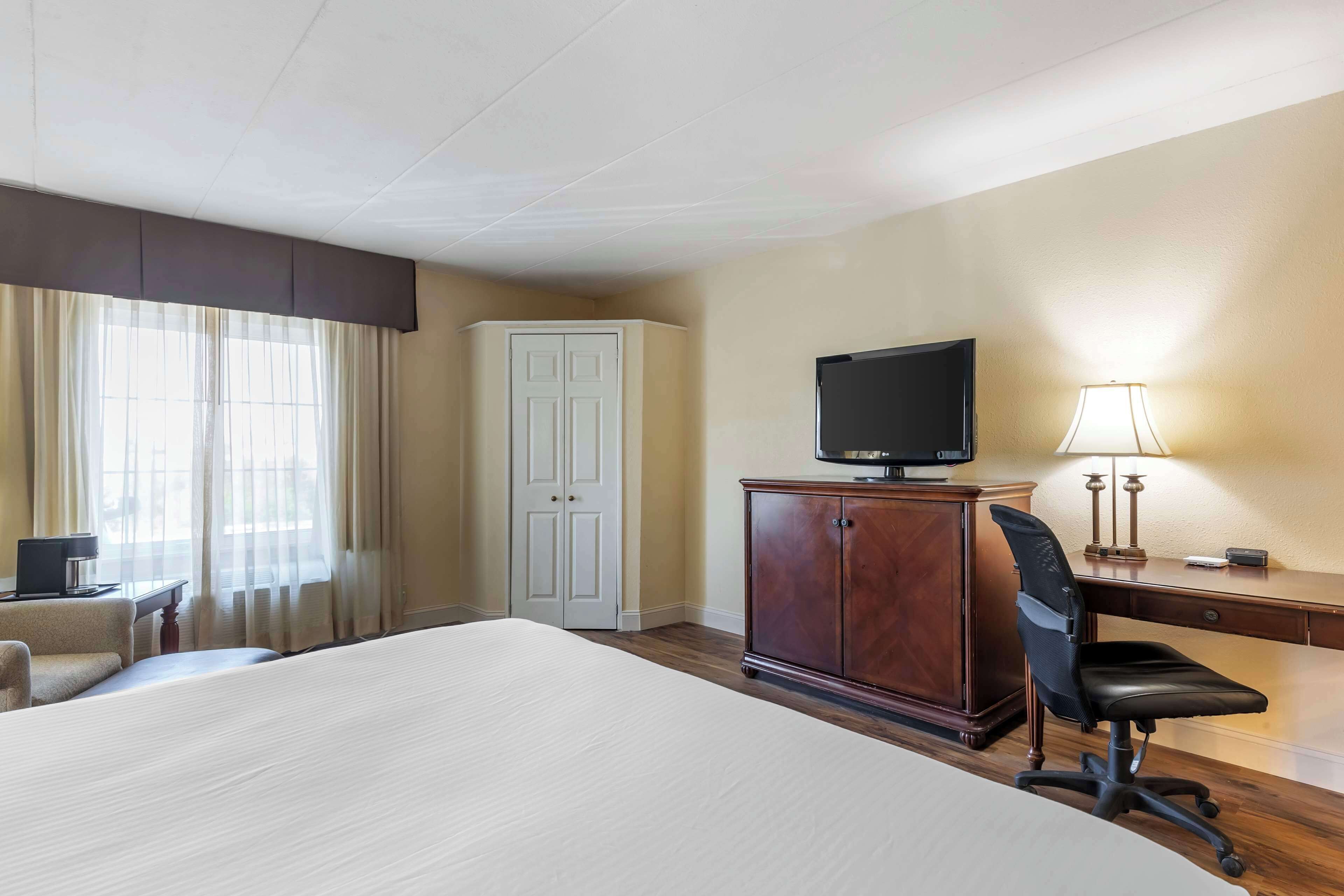 A hotel room with a large bed, a desk with a computer, a television, a wardrobe, and a chair.