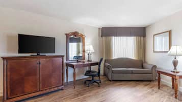 Une chambre d’hôtel avec un bureau en bois, une télévision, un canapé, une chaise et une lampe.
