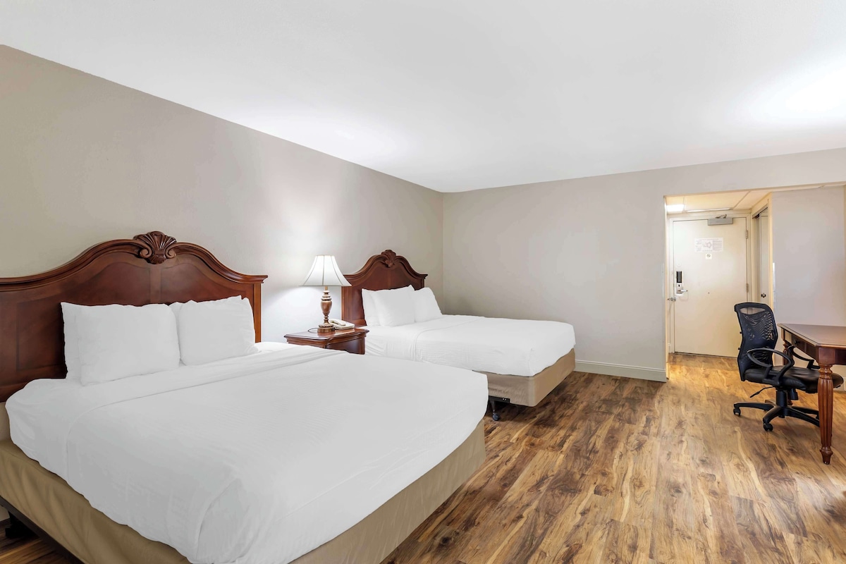 Una habitación de hotel con dos camas, un escritorio, una silla y una puerta que da a otra habitación.