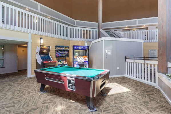 A pool table in a multi-level indoor area with arcade games and a sign indicating a 5% area charge.