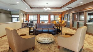 A hotel lobby with a brown leather sofa, two armchairs, a woven ottoman, and a reception desk.