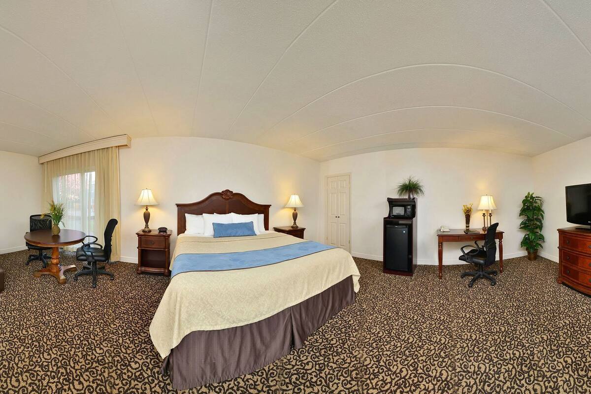 A hotel room with a large bed, a desk, a chair, a television, and a microwave.