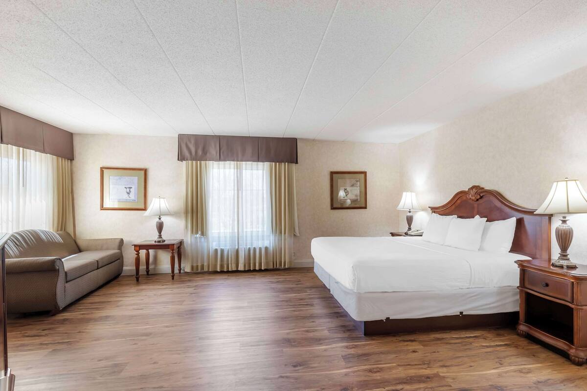 A hotel room with a large bed, a sofa, two bedside tables with lamps, and a framed picture on the wall.