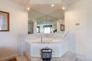 A modern bathroom with a large freestanding bathtub, a mirror above it, and a small wicker basket on the floor.