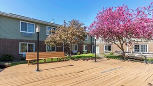 A wooden deck with a bench, a lamp post, and a pink flowering tree.
