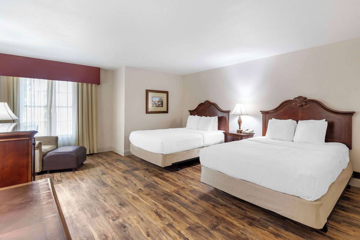 A hotel room with two beds, a desk, a chair, and a window with curtains.