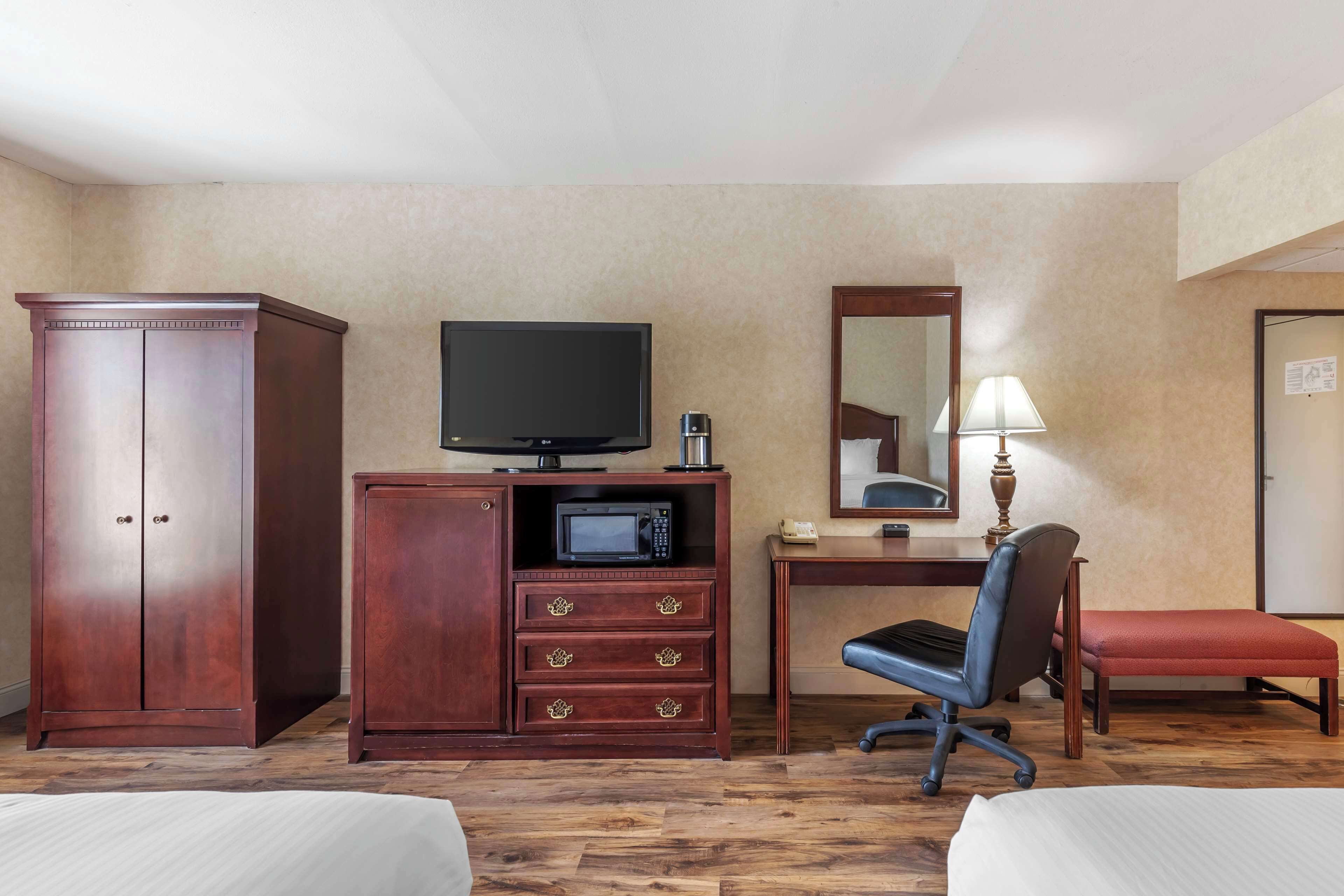 Habitación de hotel con armario de madera, escritorio con televisor, microondas, silla y cama.
