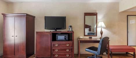 Habitación de hotel con armario de madera, escritorio con televisor, microondas, silla y cama.