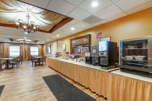 A buffet setup with a long counter, various food items, a coffee machine, and a refrigerator.