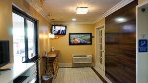 A hotel hallway with a reception desk, a television, a wall-mounted monitor, and a fire exit sign. - Howard Johnson by Wyndham Salinas (Salinas)