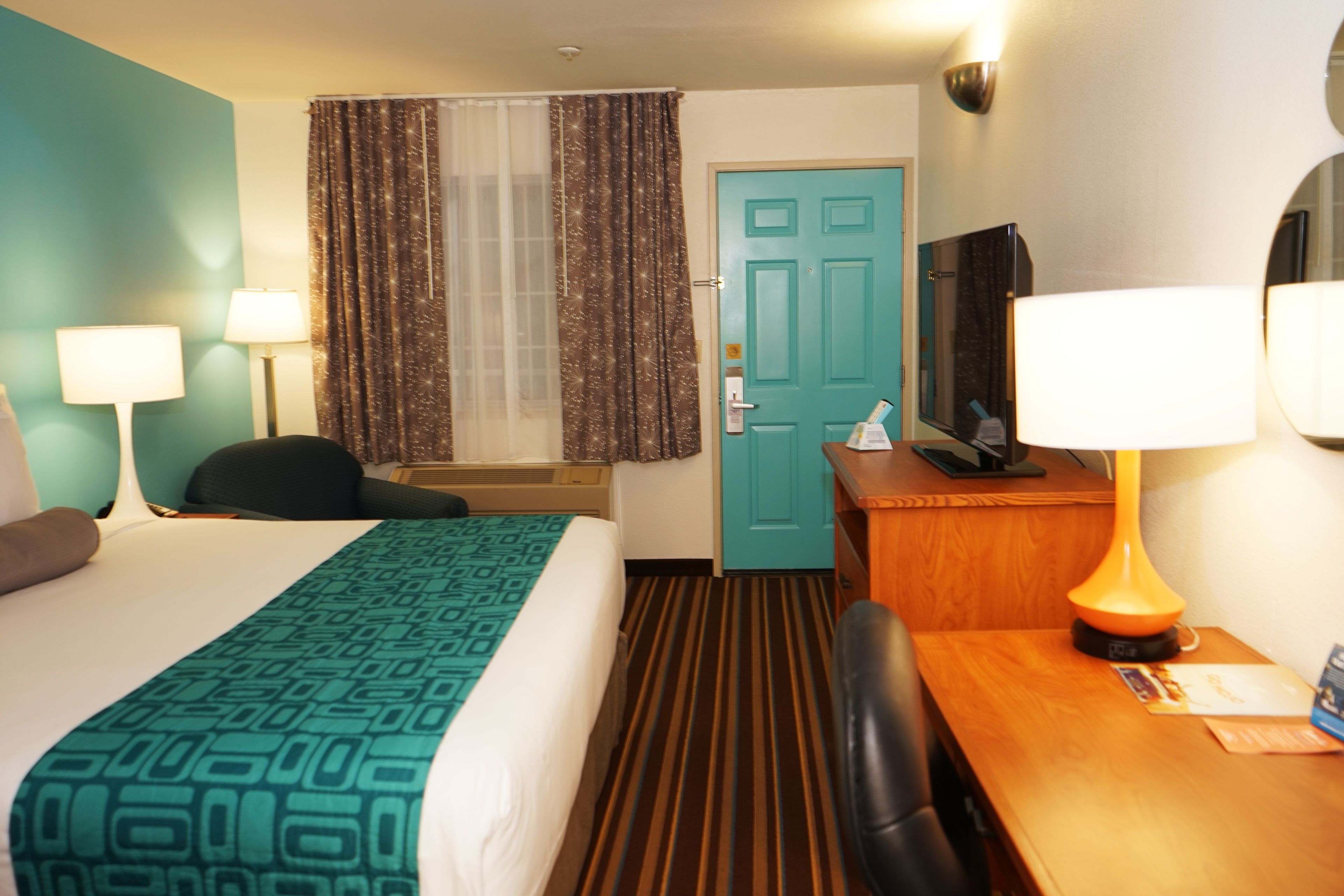 Een hotelkamer met een bed, een bureau, een stoel, een televisie, een lamp en een deur.